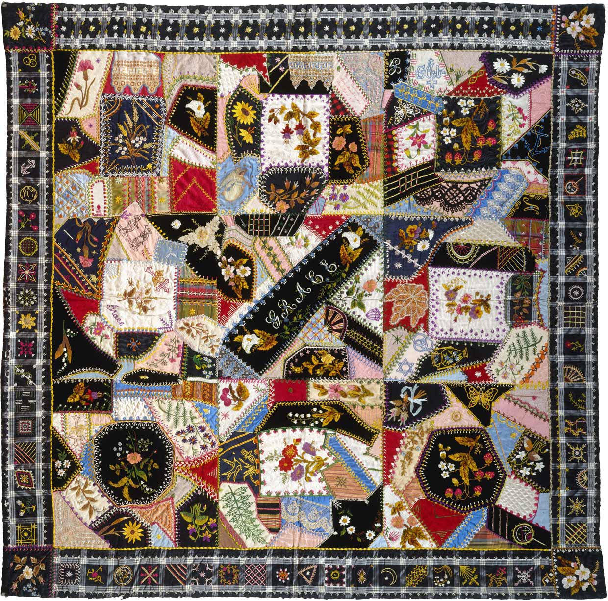 A crazy quilt full of hundreds of irregular-shaped patches stitched together with elaborate stitchings and embroidered with flowers and patterns. The word “GRACE” is embroidered in the middle.